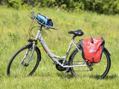 Rad+Reisen unisex Fahrrad mit Lenkertasche und Packtasche. Das Rad steht in der Wiese bei der Donauinsel.