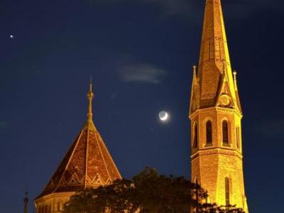 Beleuchteter Kirchturm bei Nacht mit Mondsichel im Hintergrund